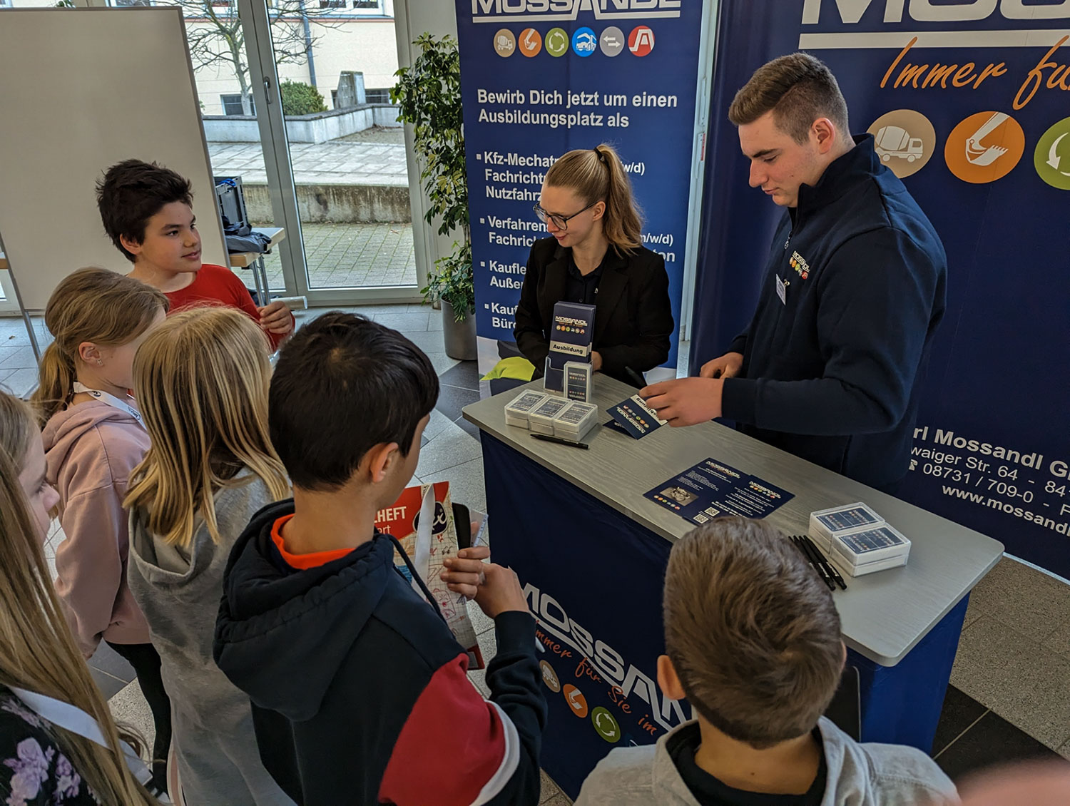 Schüler stehen um einen Stand und hören der Frau zu